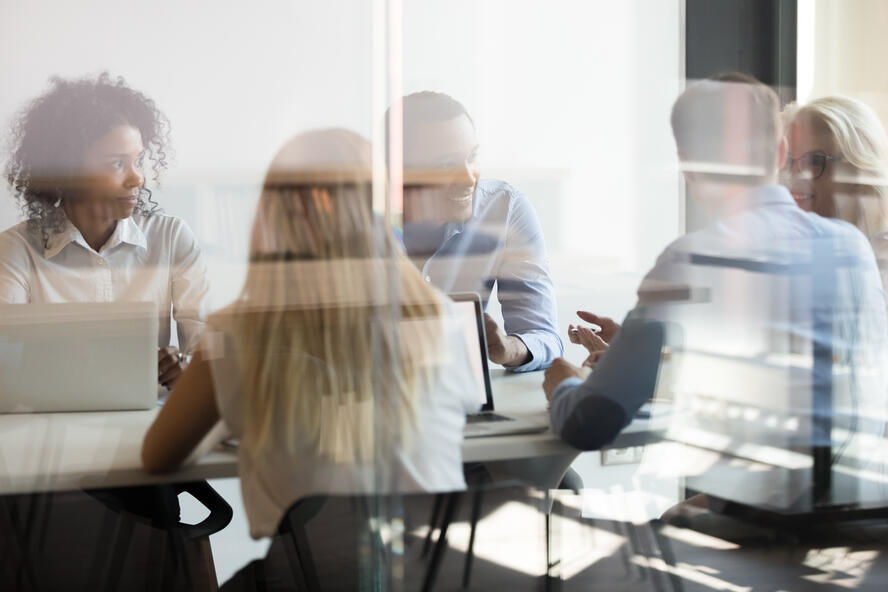 A group of people having a meeting in an office setting, behind glass door.