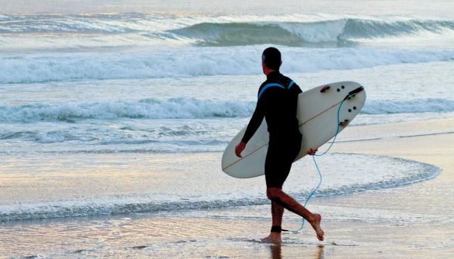 Surfer walking into ocean at sunset