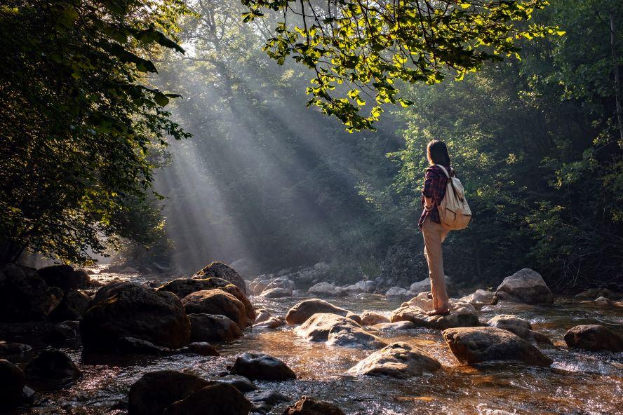 Woman in forest with backpack with sun rays peaking through trees