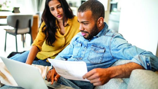 Casually dressed couple on sofa looking at computer and paper